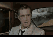 a man in a trench coat and tie is sitting in a car