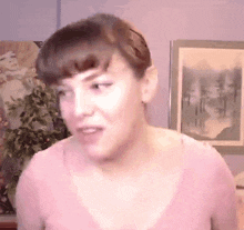 a woman in a pink shirt is making a funny face in front of a painting