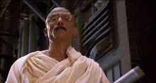a bald man wearing glasses and a white robe looks up