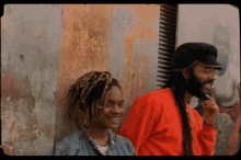 a man and a woman are leaning against a wall and the woman is smiling