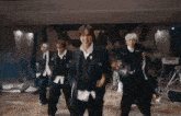 a group of men in suits are dancing in a room with chairs and a guitar