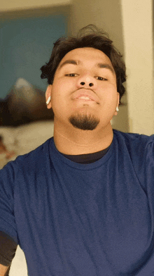 a man wearing a blue shirt and ear buds looks at the camera
