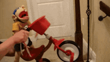 a puppet is riding a red tricycle with a person holding the handlebars