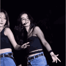 two women are dancing on a stage and one is wearing a microphone .