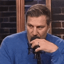 a man wearing a blue sweater and a ring is talking into a microphone