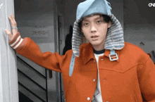a man wearing an orange jacket and a blue hat stands in front of a sign that says one on it