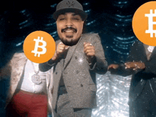 a man in a suit and hat holds a coin with the letter b on it
