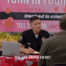 a man sitting at a table with a laptop and a sign that says " we are done here " behind him