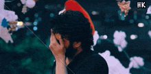 a man covering his face in front of a christmas tree with hk written on the bottom