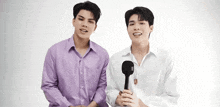 two young men in purple shirts and white shirts are standing next to each other and holding microphones .