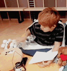 a young boy is laying on the floor playing with stuffed animals and holding a piece of paper