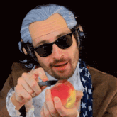 a man in a wig and sunglasses is holding a knife and an apple