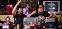 two men are standing in front of a table with a box that says satan on it
