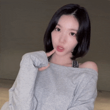 a woman wearing a grey off the shoulder sweatshirt and a black and white bra