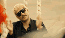 a man wearing sunglasses and a black suit looks at the camera