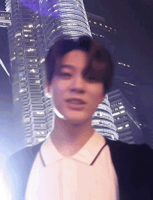 a young man in a white shirt is standing in front of a tall building at night .