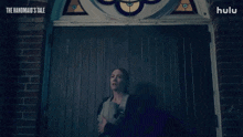 a woman holding a baby stands in front of a door that says the handmaid 's tale