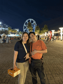 a man and a woman are posing for a photo in front of a ferris wheel