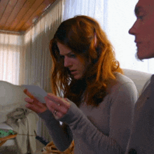 a woman with red hair is holding a piece of paper in her hand
