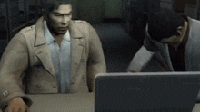 two men are sitting at a table looking at a laptop .