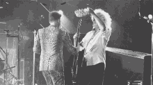 a black and white photo of a man holding a crown on a stage while another man plays a guitar .