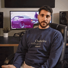 a man wearing a cheerlee college of music sweatshirt sits in front of a computer