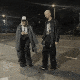 two men are walking down a street at night with one wearing a t-shirt with a picture of a man on it