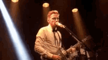 a man in a bow tie is singing into a microphone while playing a guitar on a stage .