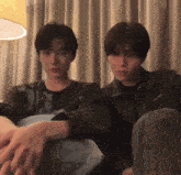 two young men are sitting next to each other on a couch in a room .