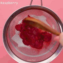 a person is sifting raspberry sauce through a strainer with a wooden spoon