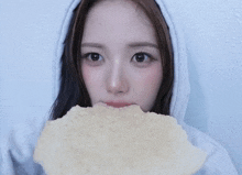 a woman in a white hoodie is holding a piece of food in front of her face