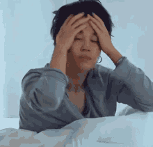 a man is laying on a bed holding his head with his hands .