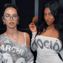 a woman holding a chicken wing next to another woman wearing a shirt that says ' socio ' on it