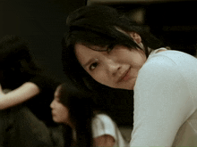 a woman in a white shirt is looking over her shoulder at the camera