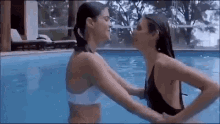 two women in bikinis are standing in a swimming pool holding hands .