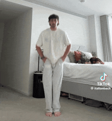 a man is standing in front of a bed with a tiktok written on the bottom