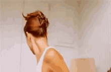 a woman in a white tank top is standing in a room and looking at something .
