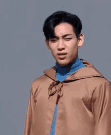 a young man in a brown jacket and blue turtleneck is making a funny face and pointing at the camera .