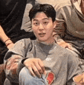 a young man in a gray sweater is sitting on a couch with his hands on his knees .