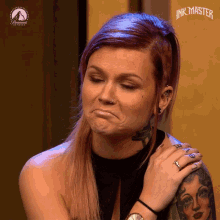 a woman with a tattoo on her arm is making a face in front of a sign that says " ink master "