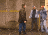 a man in a brown jacket is smoking a cigarette while two other men stand around him