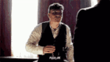 a man in a suit is sitting at a table with a glass of wine in his hand .