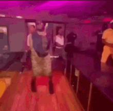 a man is dancing on a stage in a club with purple lights behind him .