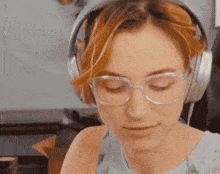 a woman wearing headphones and glasses looks down at something