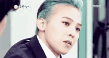 a man with blue hair is wearing a suit and tie and looking at the camera .