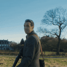 a man in a suit is holding a gun in a field with trees in the background