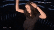 a woman in a black shirt is dancing in a dark room with a blue light behind her .