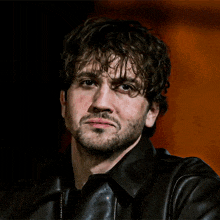 a man with curly hair and a beard wearing a black leather jacket