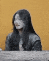 a woman with long black hair and white paint on her face is sitting at a table with her eyes closed .