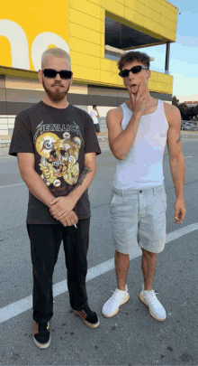 a man in a metallica shirt stands next to another man in a white tank top